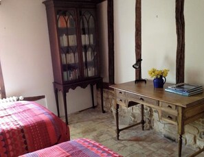 A bedroom with a wooden desk, a chair, a bed with a red and blue patterned bedspread, and a wooden cabinet.