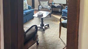 Une pièce au décor traditionnel, avec des poutres apparentes, un canapé bleu, un fauteuil à motifs, une petite table et un portrait encadré accroché au mur.