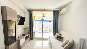 Een moderne hotelkamer met een flatscreen televisie, een bank, een tv-meubel en een glazen schuifdeur naar een balkon.