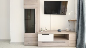 Een moderne woonkamer met een ingebouwde televisie, een houten dressoir met lades, een klein tafeltje met decoratieve objecten, en een grijze gordijn.