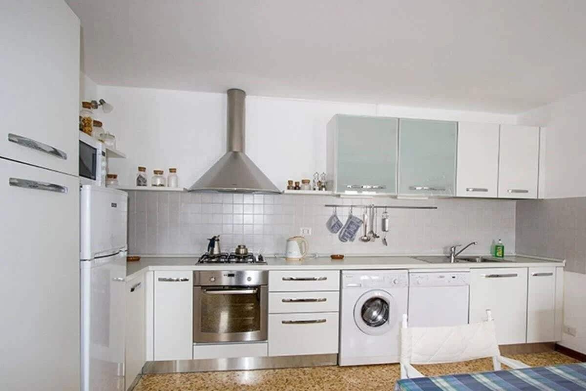 A compact kitchen with white cabinetry, a stainless steel range, a built-in oven, a washing machine, and a microwave.