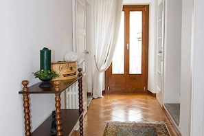 Un corridoio con una porta in legno, tende bianche, un piccolo tavolo con una pianta e un tappeto decorato.
