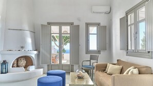 A spacious living room with a white fireplace, a beige sofa, blue ottomans, and a glass coffee table. - Modern Cycladic house with pool (Paros)