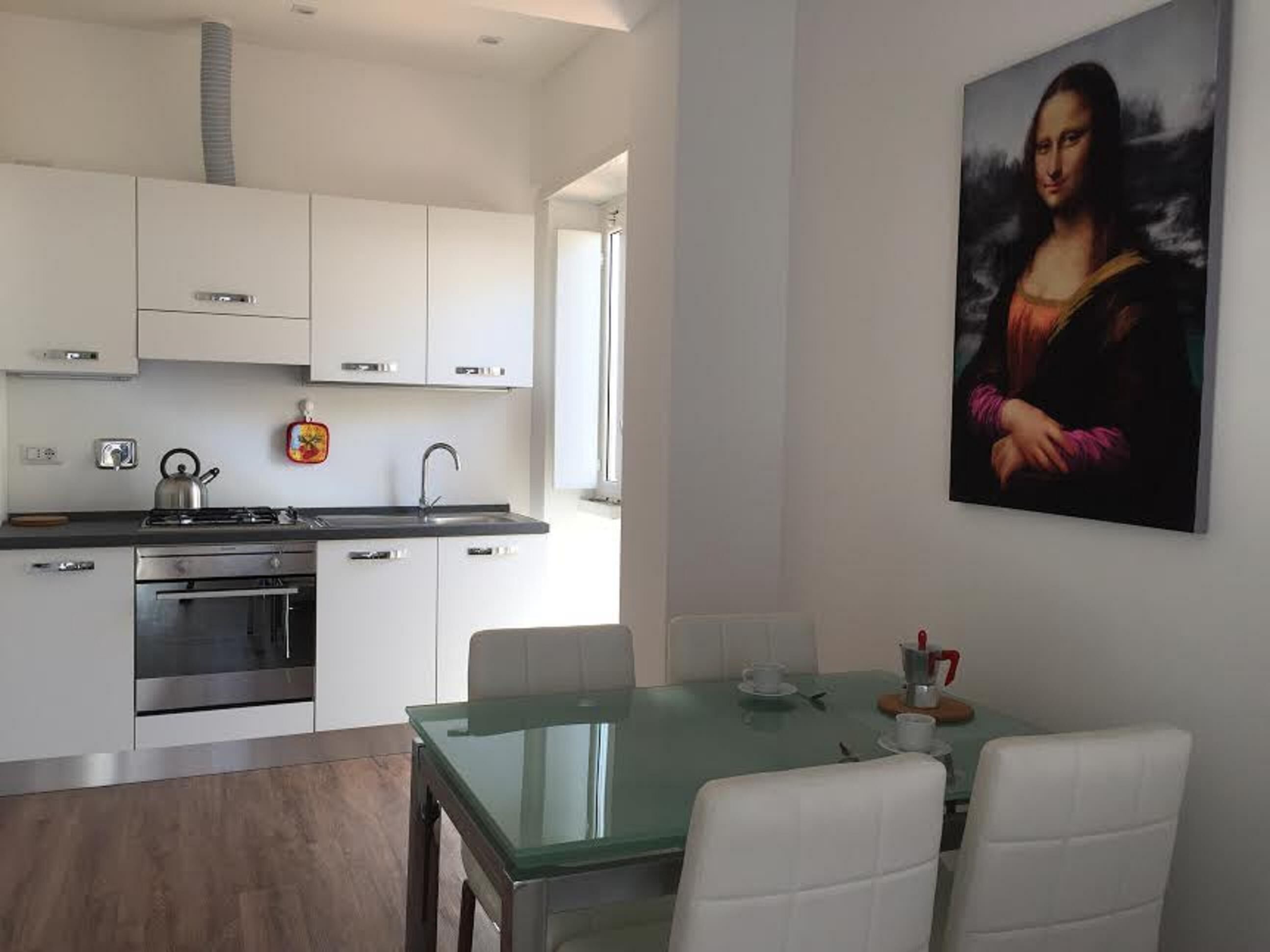A modern kitchen with white cabinets, stainless steel appliances, and a glass dining table with white chairs.