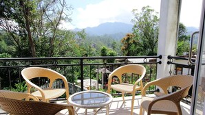 A balcony with wicker chairs and a glass table, overlooking a lush landscape with mountains in the distance. - Hotel Mevon (Bandarawela)