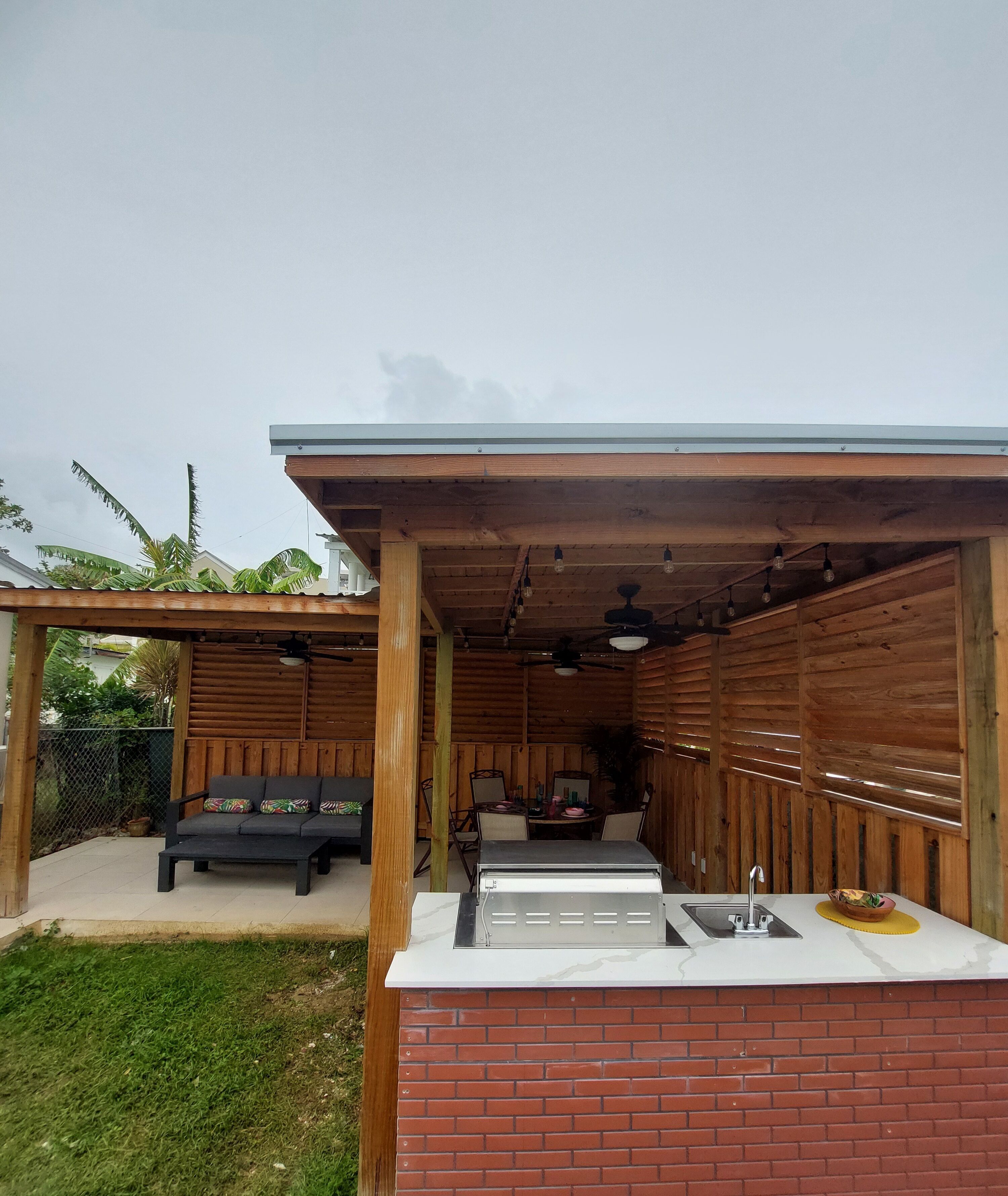 Un patio al aire libre con mostrador de ladrillo, una parrilla, una mesa de comedor y un sofá.