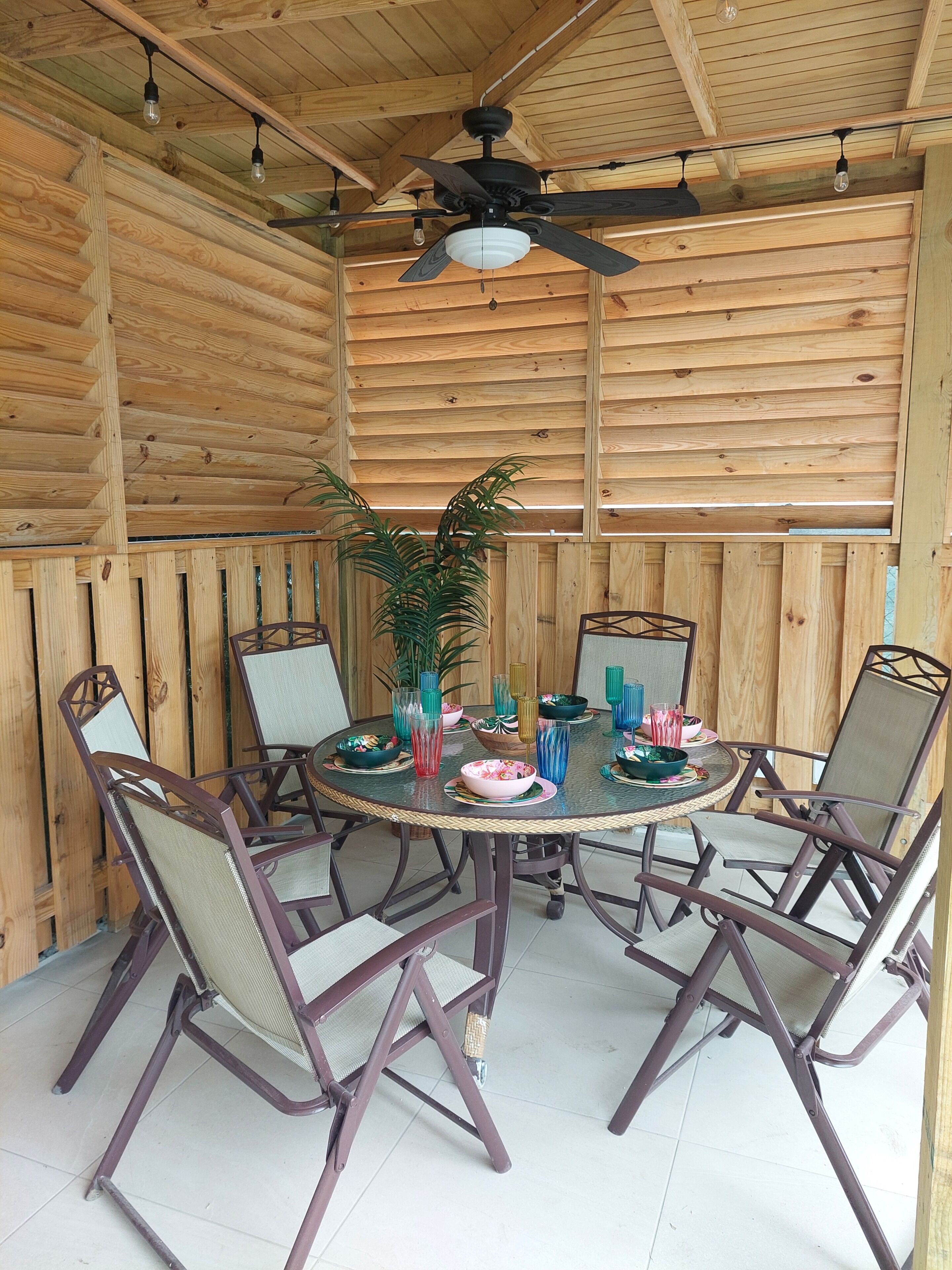 A wooden-paneled room with a round table, chairs, a ceiling fan, and hanging light bulbs.