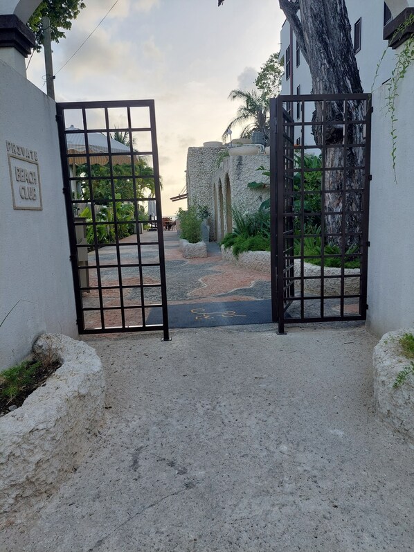Une entrée fermée par un portail, donnant accès à un club de plage privé, avec un mur en pierre et des plantes tropicales.