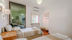 A hotel room with two beds, a sitting area with a chair and a table, a window with a view, and an air conditioning unit. - Italian Lakes lakeside villa with direct lake access (Ranco)