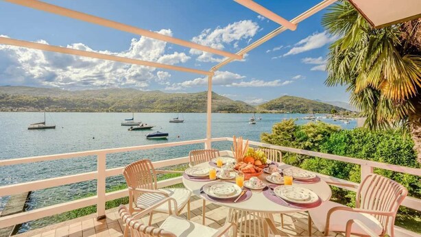 A terrace with a table set for dining, overlooking a body of water with boats. - Italian Lakes lakeside villa with direct lake access (Ranco)