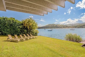 A poolside area with lounge chairs and a view of a lake with boats. - Italian Lakes lakeside villa with direct lake access (Ranco)