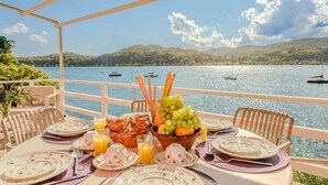 An outdoor dining area with a table set for breakfast, overlooking a lake with boats. - Italian Lakes lakeside villa with direct lake access (Ranco)