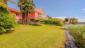 A house with a red exterior, a balcony, and a well-maintained lawn. - Italian Lakes lakeside villa with direct lake access (Ranco)