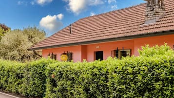 Un bâtiment avec un toit recouvert de tuiles rouges, une façade rose et une haie bien entretenue à l’avant.