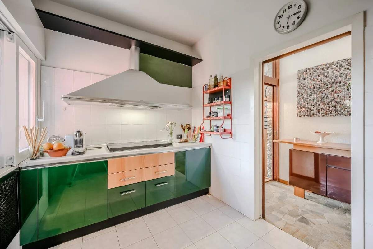Eine moderne Küche mit grünen Schränken, einer Edelstahl-Dunstabzugshaube und einem roten Regal mit Küchenutensilien.