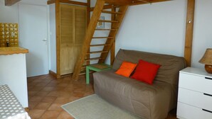 A cozy room with a wooden ceiling, a sofa with orange pillows, a small table, and a green chair. - studios - 1 room - 2/4 persons (Annecy)