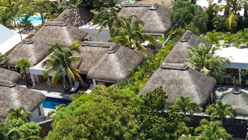 Un complexe hôtelier doté de bungalows aux toits de chaume, entourés d’une végétation luxuriante et comprenant une piscine.