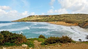 A coastal landscape with a beach, rocky terrain, and a clear sky. - Tal-barun Farmhouse (San Lawrenz)