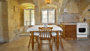 A rustic kitchen with a wooden table set for dining, a built-in oven, and stone walls. - Tal-barun Farmhouse (San Lawrenz)