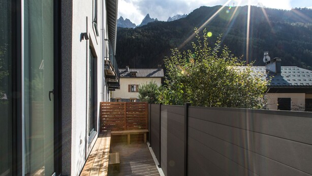 A narrow outdoor corridor with a wooden bench and a view of a mountain range. - Spacious Central Apartment with Terrace (Chamonix-Mont-Blanc)