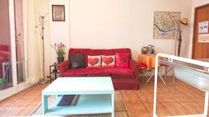 Una sala de estar con un sofá rojo, una mesa de centro blanca, una mesa de comedor con sillas, un mapa en la pared y un sombrero en un perchero.