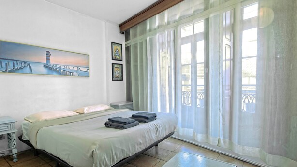 Habitación de hotel con cama, un cuadro, una ventana con cortinas y vista a un balcón.