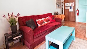 Una sala de estar con un sofá rojo, una mesa de centro azul, una mesita con un mapa y una puerta con extintor.