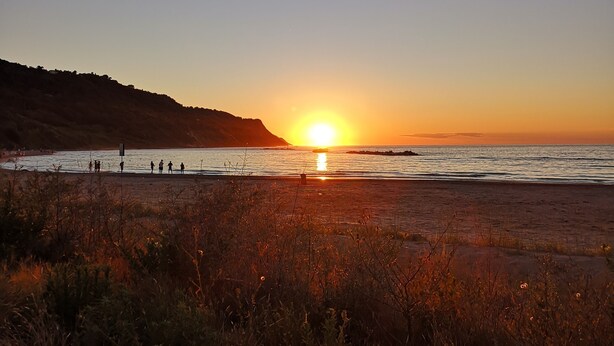 Un atardecer sobre una playa con gente caminando por la orilla.