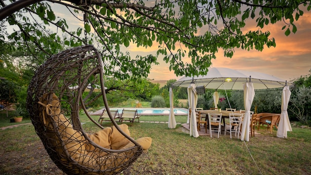 Un jardín con una silla colgante, una piscina y un área de comedor cubierta.