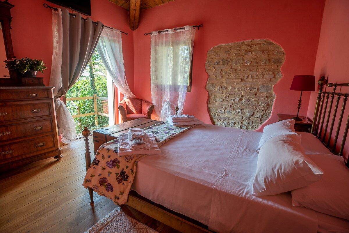 Une chambre à coucher avec un lit en bois, une commode, une chaise et une fenêtre avec des rideaux.