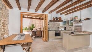A modern kitchen with wooden beams, a central island, and a dining area with a table and chairs. - Can Bons Aires by SunVillas Mallorca (Pollença)