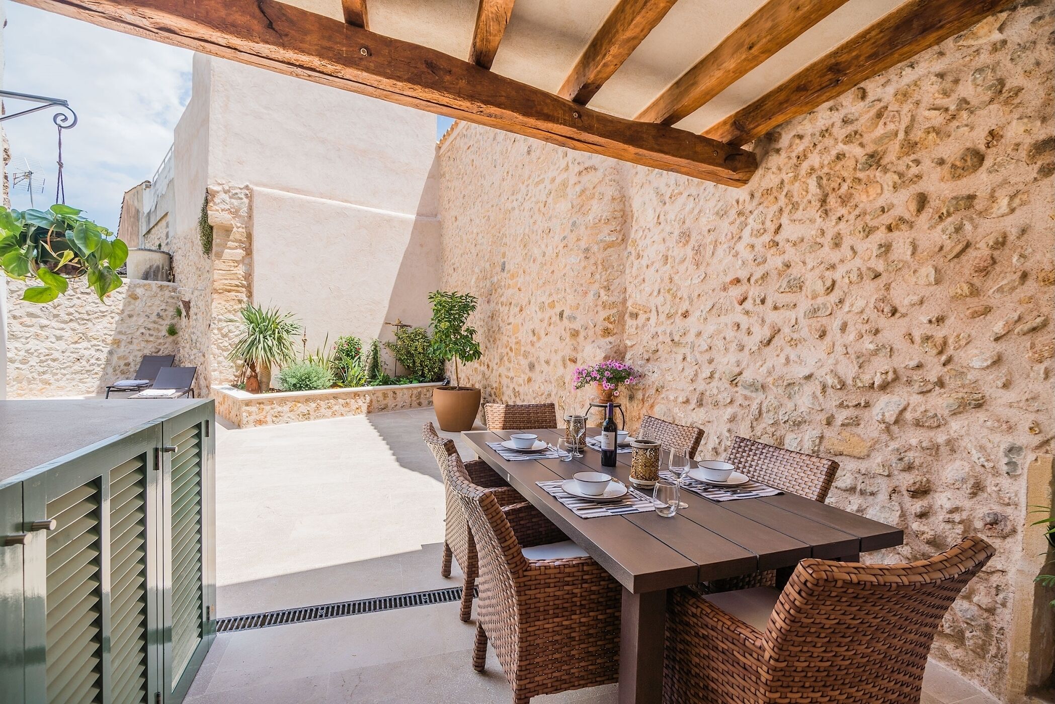 An outdoor dining area with a stone wall backdrop, wicker furniture, and a table set for four.