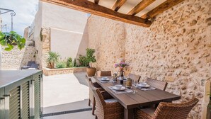 An outdoor dining area with a stone wall backdrop, wicker furniture, and a table set for four. - Can Bons Aires by SunVillas Mallorca (Pollença)