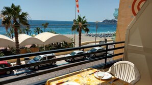 A balcony with a table set for two, overlooking a beach with umbrellas and palm trees. - Apartment Neptune at the beach with a sea view - Letojanni, Sicily (Letojanni)