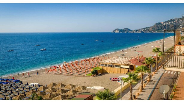 A beach with rows of umbrellas and sun loungers, a wooden building with a sloped roof, and a clear view of the sea and distant hills. - Apartment Neptune at the beach with a sea view - Letojanni, Sicily (Letojanni)
