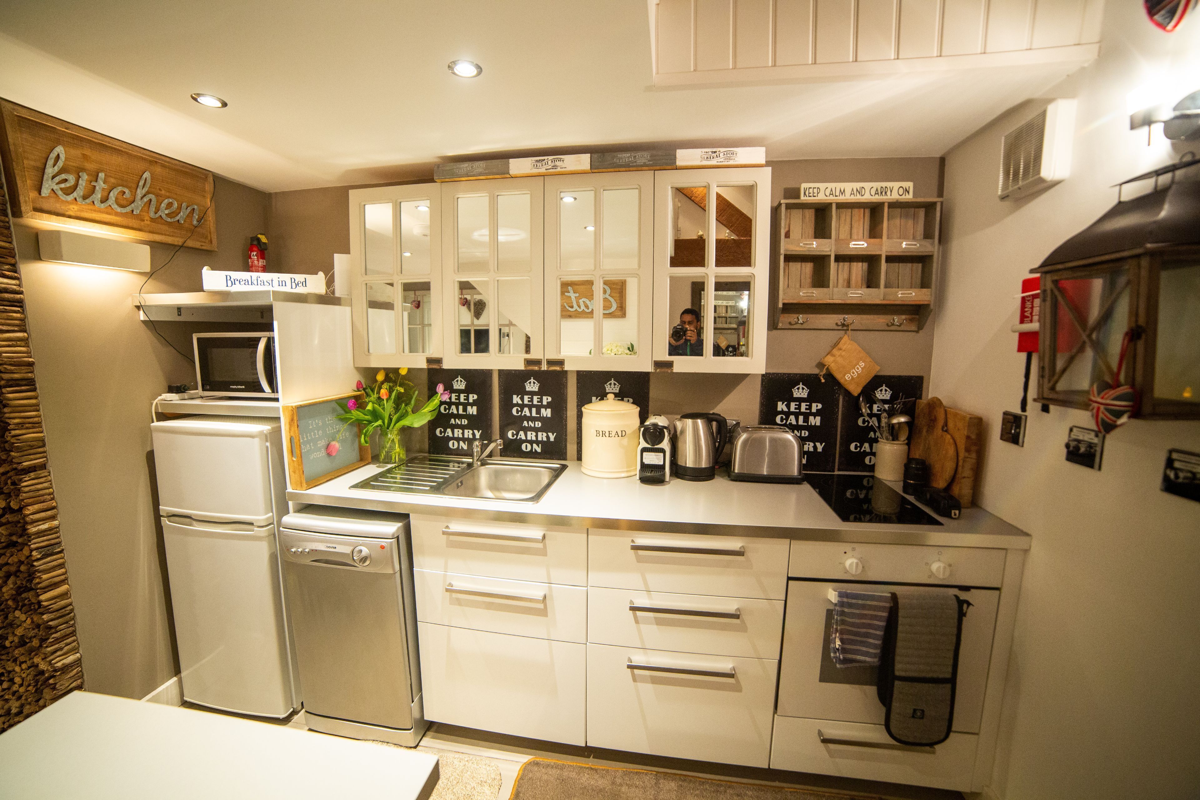 Una cocina moderna con armarios blancos, microondas integrado, refrigerador y cafetera.