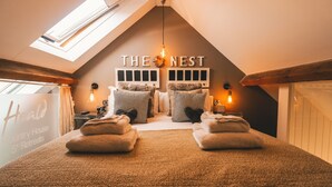 Une chambre confortable avec un plafond en pente, deux lits avec des oreillers à rayures, une horloge murale et une pancarte sur laquelle on peut lire « LE NID ».