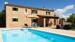 Un edificio de piedra con piscina, mobiliario exterior y una pérgola.