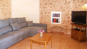 Una sala de estar con un sofá seccional gris, una mesa de centro de madera con un jarrón de flores, una estantería y un televisor sobre un mueble de madera.