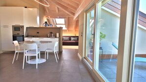 A modern kitchen with white cabinetry, a dining area with white chairs, and a large sliding glass door leading to an outdoor space.