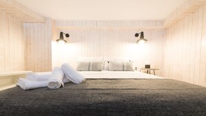 Une chambre avec un grand lit, deux lampes de chevet, une petite table et des serviettes enroulées posées sur le sol.