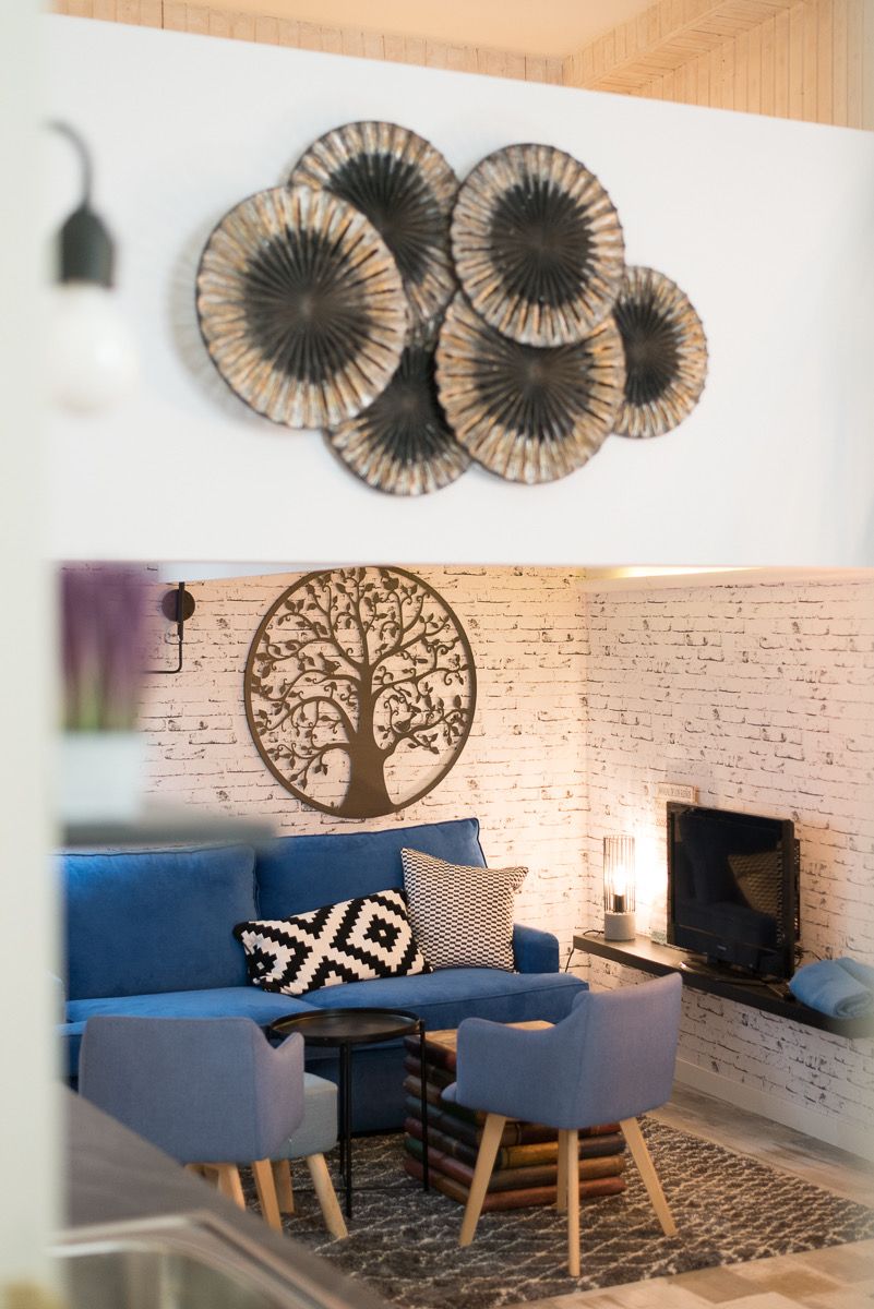 Un salon moderne avec un canapé bleu, une table basse ronde et un téléviseur. Des œuvres d'art décoratives sont accrochées au mur au-dessus du canapé.