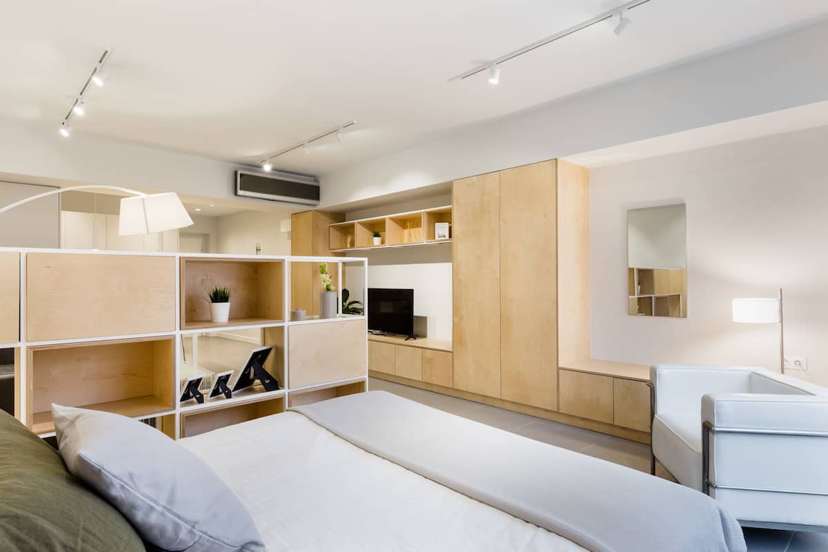A modern bedroom with a bed, a TV, built-in shelving, and a desk area.