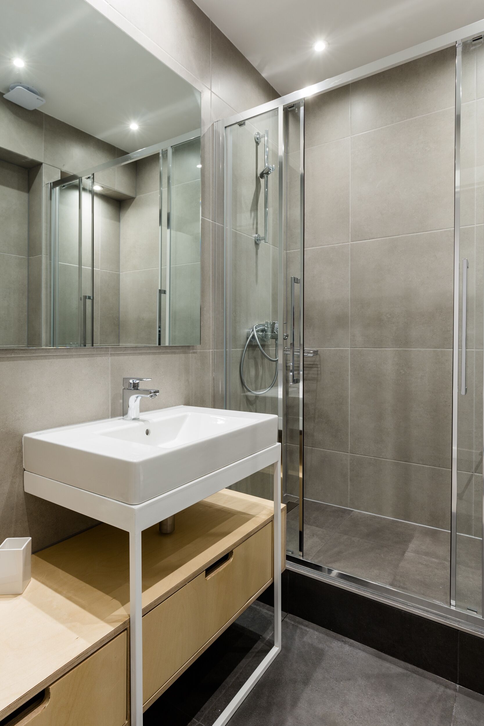 Un baño moderno con lavamanos blanco, espejo y cabina de ducha de vidrio.
