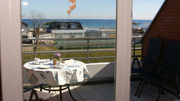 Een balkon met een eettafel, met uitzicht op een kustgebied met gebouwen en een heldere lucht.