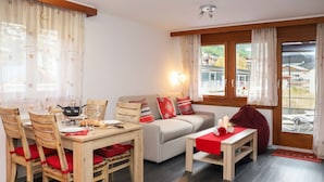 En hyggelig stue med et træspisebord, to træstole, en sofa og et sofabord med en rød bordløber.