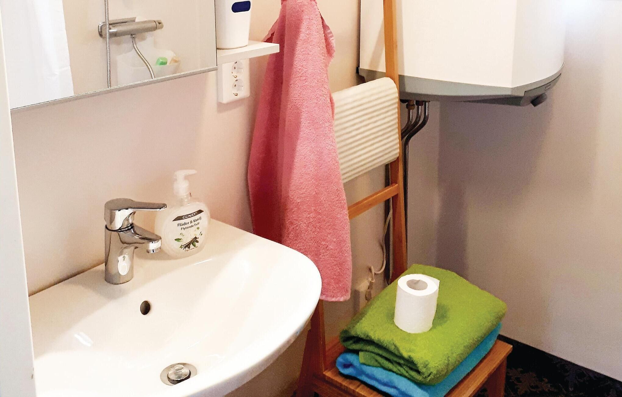 A bathroom with a sink, a mirror, a towel rack with a pink towel, a toilet paper holder with a green towel, and a white toilet.