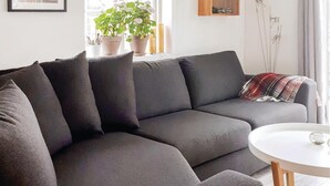 A modern living room with a dark grey sectional sofa, a round white coffee table, and a window with potted plants. - Nice home in Skillingaryd with kitchen (Skillingaryd)