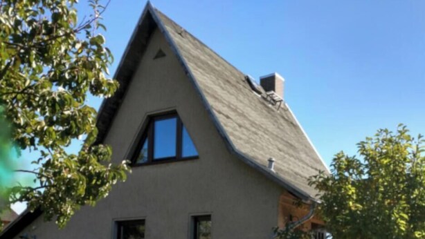 Ein Haus mit geneigtem Dach, einer kleinen Veranda und einem Garten mit Tisch und Stühlen.