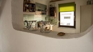 Eine Küche mit zwei Gläsern auf einem Regal, einem Fenster mit grüner Jalousie und einem Kühlschrank.